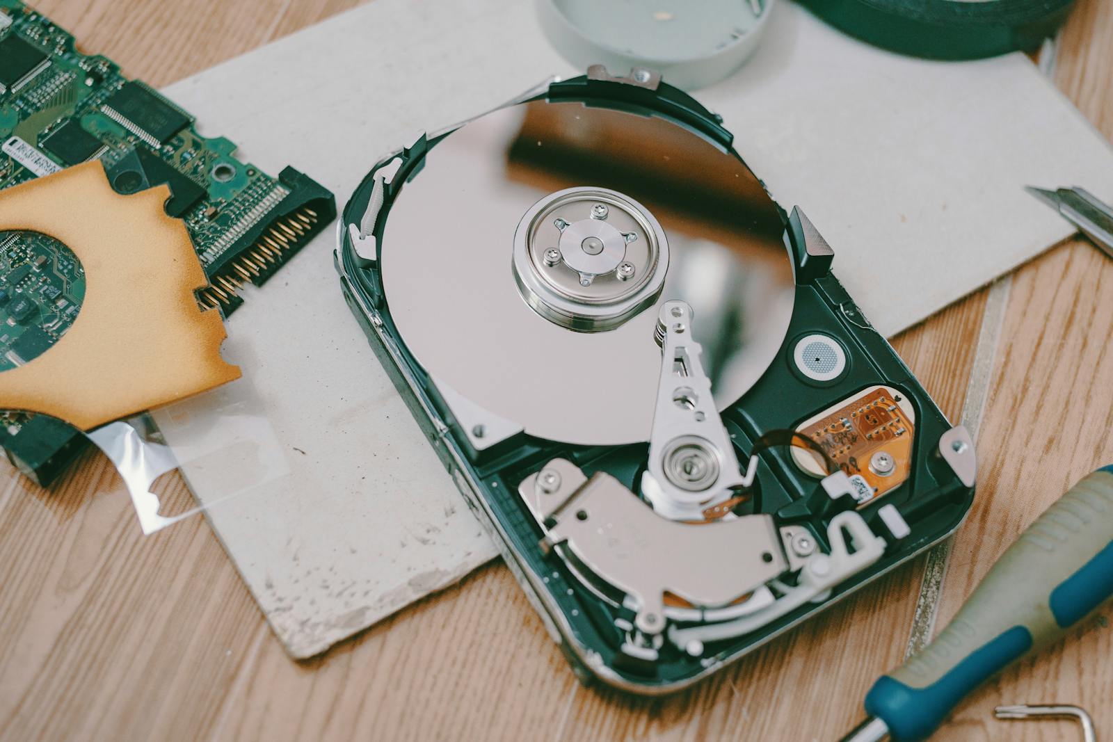 Close-up of a disassembled hard drive showing internal components on a wooden table.